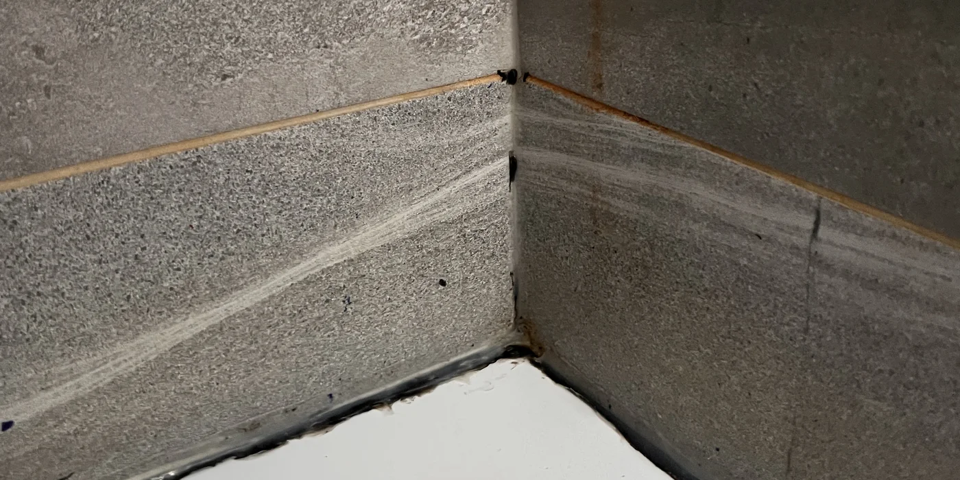 Mouldy, blown silicone in a shower corner before resealing