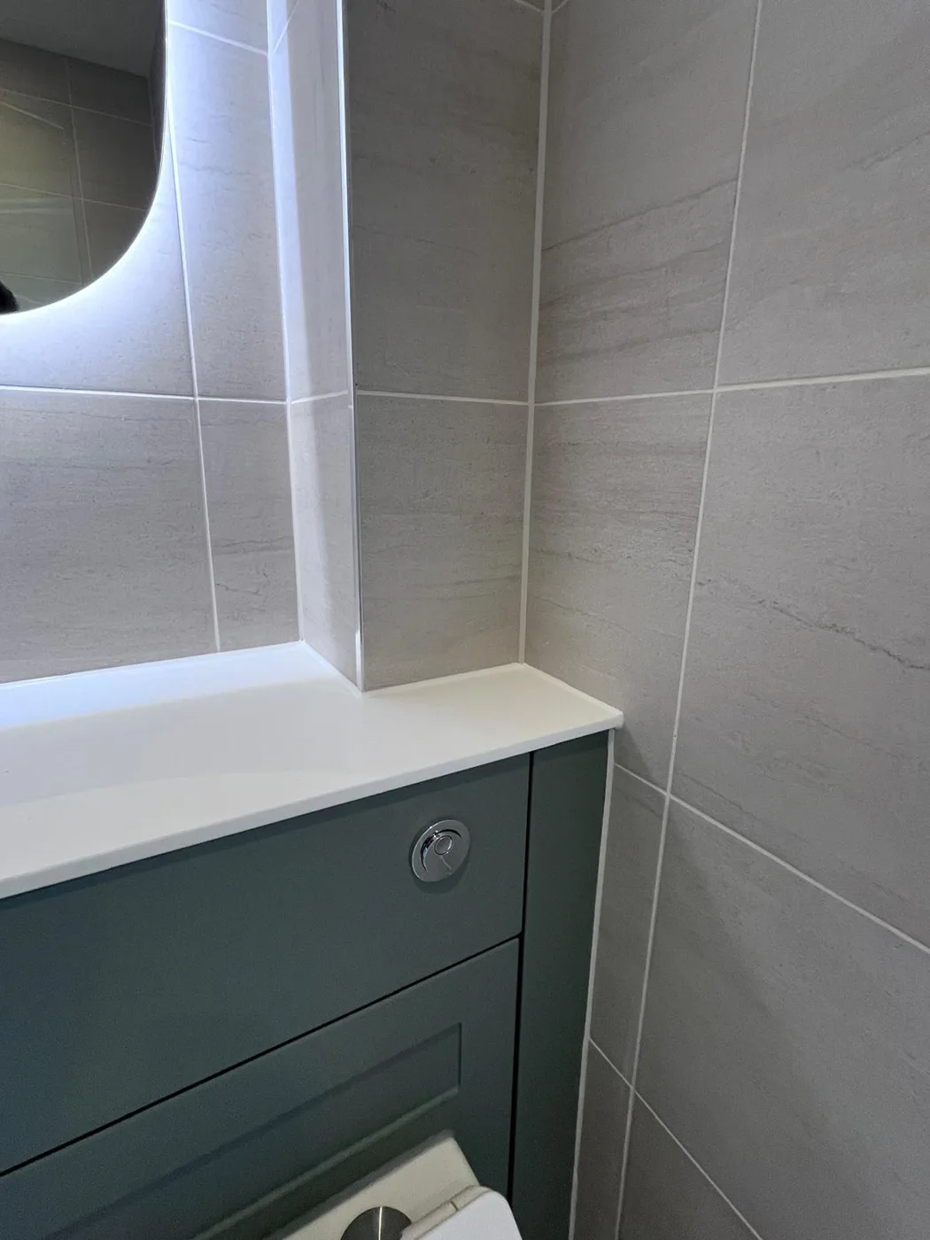 Neat sealant where grey wall tiles meet a white worktop above a green WC unit